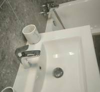 Waschbecken und Badewanne im Badezimmer eines Einzimmerapartments mit grauen Fliesen.
