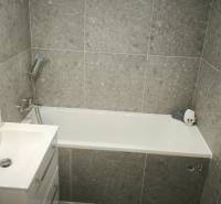Badezimmer in einem Studio-Apartment mit Badewanne, Waschbecken und grauen Fliesen.