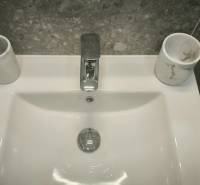 Weißes Waschbecken-Set in einem Studio-Apartment mit grauen Fliesen und einem Wasserhahn aus Metall.