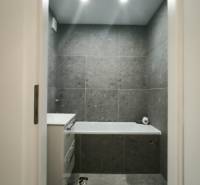 Ein Badezimmer in einem Studio-Apartment mit Wänden, die mit dunklen Fliesen verkleidet sind, und einer Badewanne.