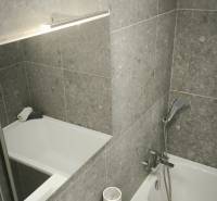Badezimmer mit Badewanne und Waschbecken in einer Einzimmerwohnung mit grauen Fliesen.