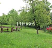 Der Garten des Einfamilienhauses Brekova mit einer hölzernen Sitzecke und Bäumen auf einer Rasenfläche.