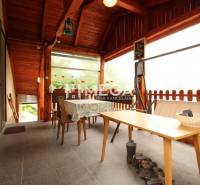 Veranda in einem Einfamilienhaus mit Holzdecke, Tisch, Stühlen und Blumen.