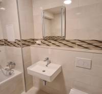 Badezimmer in einer Einzimmerwohnung mit Badewanne, Waschbecken und Toilette, Fliesen mit dekorativem Streifen.
