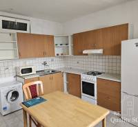 Küchenbereich einer 2-Zimmer-Wohnung mit Kühlschrank, Waschmaschine und Herd, Holztisch mit Stuhl.