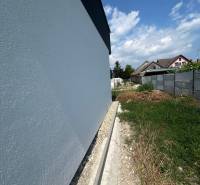 Die Wand eines Einfamilienhauses in Žihárec mit angrenzendem Grundstück unter blauem Himmel.