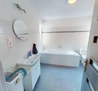 Ein Badezimmer in einem Einfamilienhaus mit Badewanne, Spiegel und Waschbecken, helle Fliesen.