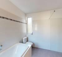 Ein Badezimmer in einem Einfamilienhaus mit Badewanne, Dusche und Toilette, gefliest mit hellen Fliesen.