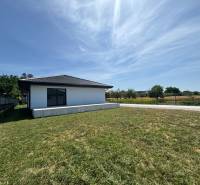 Ein Einfamilienhaus in Podlužany mit einem großen Rasen, neben einem Feldweg und einem Zaun.