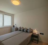 Schlafzimmer mit Bett, Schrank und Fenstern in einer Einzimmerwohnung, neutrale Farben.