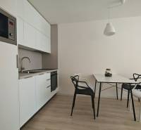 Küchenecke in einer Einzimmerwohnung, weiße Schränke, Tisch mit Stühlen, Holzboden.