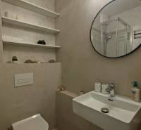 Badezimmer in einer Einzimmerwohnung mit rundem Spiegel, Waschbecken und Toilette.