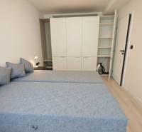 Schlafzimmer in einer Einzimmerwohnung mit zwei Betten, Einbauschrank und Nachttischlampe.