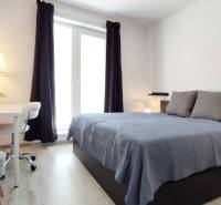 Helles Schlafzimmer in einer 2-Zimmer-Wohnung mit Bett, Tisch und Fenster mit Vorhängen.
