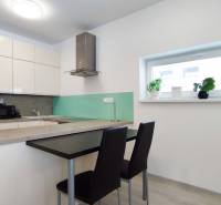 Küche in einer 2-Zimmer-Wohnung mit Bartresen, Stühlen und dekorativen Pflanzen auf der Fensterbank.