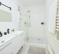Badezimmer mit weißem Waschtischunterschrank, gläserner Duschkabine und Handtuchheizkörper.