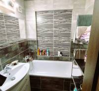 Badezimmer in einer 2-Zimmer-Wohnung mit Badewanne, Waschbecken und einem Regal mit Handtüchern.