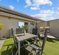 Die Terrasse einer 4-Zimmer-Wohnung mit Tisch und Stühlen, umgeben von Pflanzen und Liegestühlen.