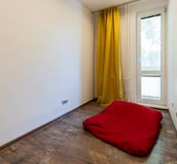 Ein Zimmer mit gelben Vorhängen, einer roten Matratze und Holzboden in einer Vierzimmerwohnung.