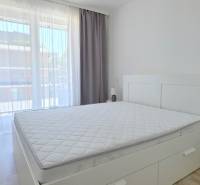 Helles Schlafzimmer mit großem Fenster, Bett und Nachttisch in einer 2-Zimmer-Wohnung.