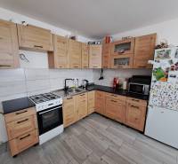 Eine Küche in einem Einfamilienhaus mit hellen Holzschränken, einem weißen Kühlschrank und einem Elektroherd.