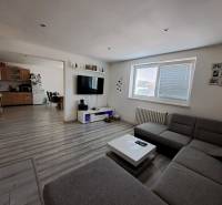 Wohnzimmer mit Küche in einem Einfamilienhaus mit Sofa, Fernseher und Holzschränken.