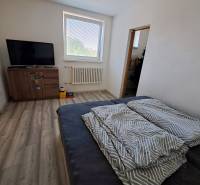Ein Zimmer in einem Einfamilienhaus mit einem Fernseher, einem Sofa und einem Fenster, das natürliches Licht hereinlässt.