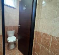 Toilette mit geschlossener Tür in Geschäftsräumen, gefliest mit braunen Fliesen.