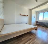 Schlafzimmer in einer 2-Zimmer-Wohnung mit Holzboden, Bett und Sessel.