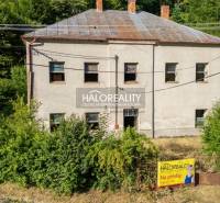 Ein zweistöckiges Gebäude in Hodruša - Hámre, umgeben von Grün, mit einem Immobilienbanner am Zaun.
