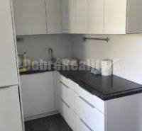 Küche in einer 2-Zimmer-Wohnung mit weißen Schränken und dunkler Arbeitsplatte.