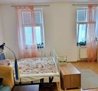 Innenraum einer Einzimmerwohnung mit Bett, Holzboden und Fenstern mit rosa Vorhängen.