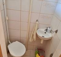 Toilette und Waschbecken im Badezimmer einer Einzimmerwohnung mit beigen Fliesen.