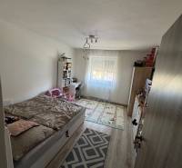 Schlafzimmer mit Bett und Bücherregal in einer 3-Zimmer-Wohnung, heller Boden, dekorativer Teppich.