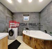 Badezimmer mit Badewanne und Waschmaschine in einem Einfamilienhaus. Graue Wände mit hellen Böden.