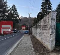 Ein Weg mit einem Gehsteig, der durch Pezinok an einem Einfamilienhaus vorbeiführt, im Hintergrund eine hügelige Landschaft.
