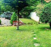 Garten eines Einfamilienhauses in Píla mit Bäumen, Rasen und Steingarten.