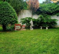 Der Garten eines Einfamilienhauses in der Gemeinde Píla mit Rasen, einer Statue und einer Bank an der Wand.