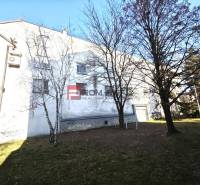 Ein Gebäude mit Grünflächen und Bäumen in der Ľ. Podjavorinská Straße, im Hintergrund ein blauer Himmel.