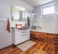 Ein Badezimmer in einem Einfamilienhaus mit einer Badewanne, einem weißen Waschbecken und einem braunen Boden.