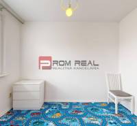 Ein leerer Raum mit einem bunten Teppich, einem Stuhl und einer Kommode in einer 4-Zimmer-Wohnung.