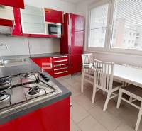 Die Küche einer 4-Zimmer-Wohnung mit roten Schränken, einem Gasherd und einem Esstisch.