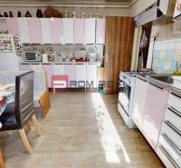 Küche in einem Einfamilienhaus mit weißen und rosa Schränken, Esstisch und Herd.