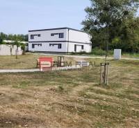 Ein Einfamilienhaus in Dunajská Streda mit einem großen Rasenstück und Bäumen am Rand.