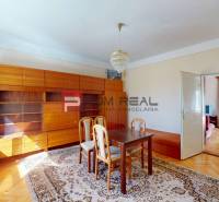 Esszimmer eines Einfamilienhauses mit Holzmöbeln, Teppich und Kronleuchter, verbunden mit dem Wohnzimmer.