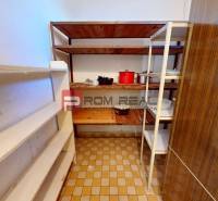 Speisekammer in einem Einfamilienhaus mit flachen Regalen und Töpfen auf dem Fliesenboden.
