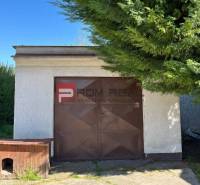 Auf dem Bild ist ein kleines weißes Häuschen mit einer Garage in der Mitte, umgeben von Grün.