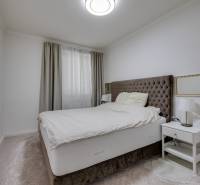 Schlafzimmer in einer 3-Zimmer-Wohnung mit einem bequemen Bett, einem Nachttisch und Vorhängen.