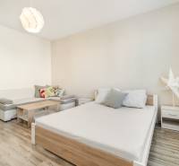 Helles Zimmer mit Bett, Sofa und Ventilator in einer Einzimmerwohnung.