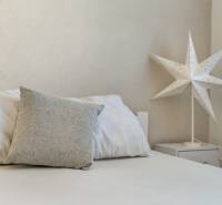 Bett mit grauem Kissen und dekorativem Papierstern am Tisch.